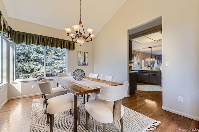 dining room featuring hardwood / wood-style flooring, vaulted ceiling, sink, and a chandelier