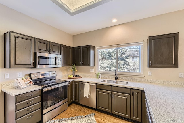 kitchen with appliances with stainless steel finishes, light hardwood / wood-style floors, sink, and dark brown cabinets