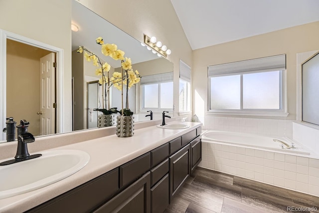 bathroom with vanity, vaulted ceiling, wood-type flooring, and tiled tub