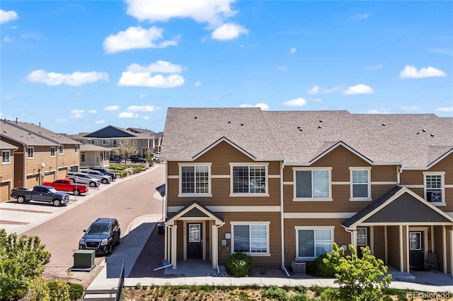 multi unit property featuring a residential view, cooling unit, a shingled roof, and uncovered parking