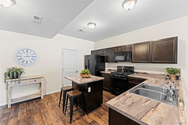 kitchen featuring black appliances, a sink, a center island, dark brown cabinetry, and a breakfast bar