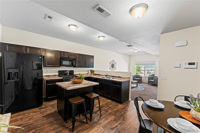 kitchen featuring black appliances, a sink, dark wood-type flooring, a textured ceiling, and a kitchen island