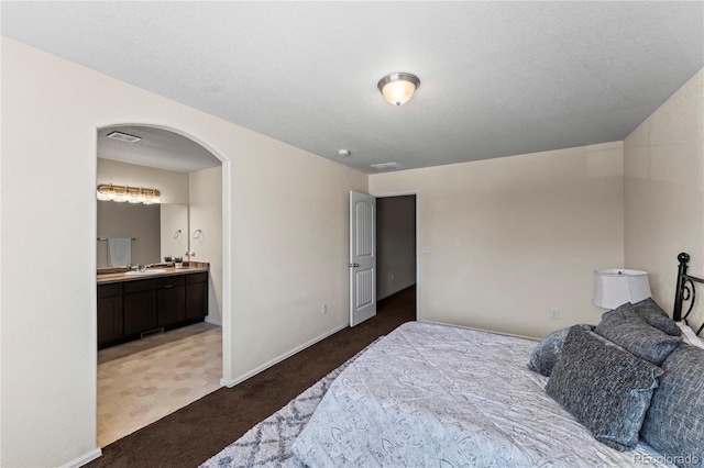 carpeted bedroom featuring arched walkways, a sink, baseboards, and connected bathroom