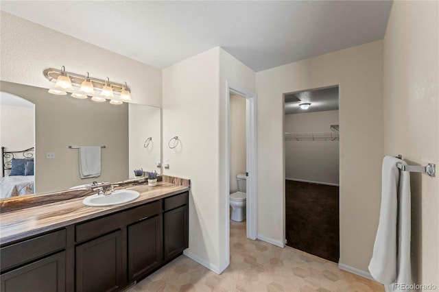 bathroom with baseboards, vanity, toilet, a walk in closet, and connected bathroom