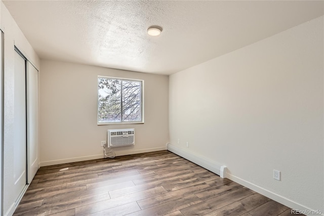 1302 S Parker Rd Unit 229, Denver, CO 80231 - unfurnished bedroom with wood finished floors, a textured ceiling, a wall mounted AC, a closet, and baseboards