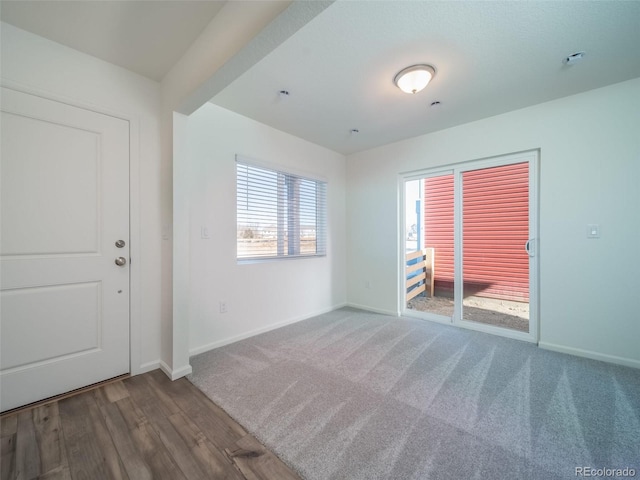 carpeted spare room featuring baseboards and wood finished floors