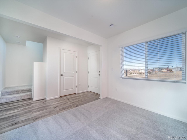 carpeted spare room with wood finished floors, baseboards, and stairs