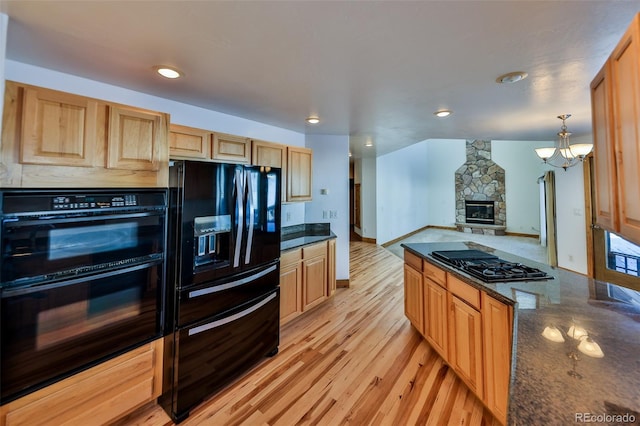 kitchen featuring pendant lighting, a fireplace, dark stone countertops, light hardwood / wood-style floors, and black appliances