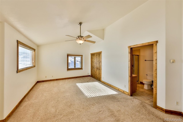 unfurnished bedroom featuring vaulted ceiling, light carpet, ceiling fan, and ensuite bath