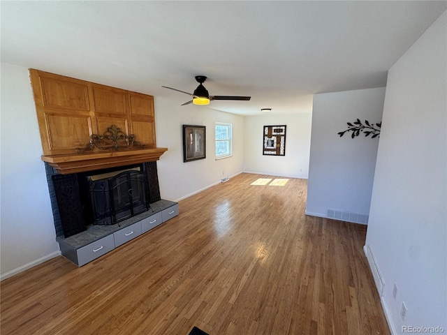 unfurnished living room featuring visible vents, light wood-style floors, ceiling fan, a tile fireplace, and baseboards