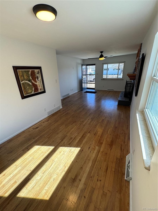 unfurnished living room featuring a fireplace with raised hearth, a ceiling fan, visible vents, baseboards, and hardwood / wood-style floors