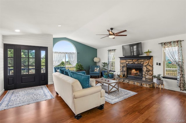 living room with a ceiling fan, vaulted ceiling, a stone fireplace, wood finished floors, and baseboards