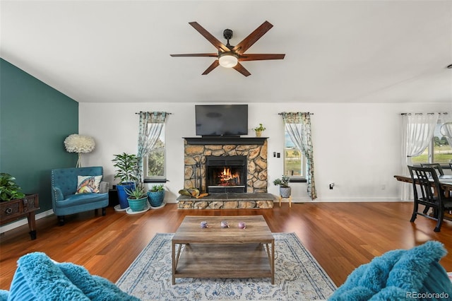 living room featuring ceiling fan, a stone fireplace, wood finished floors, and a healthy amount of sunlight