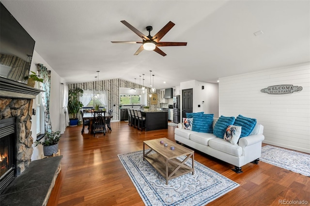 living area featuring lofted ceiling, a fireplace, dark wood finished floors, and a ceiling fan