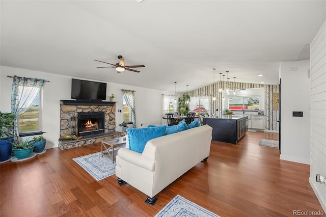 living area with vaulted ceiling, a fireplace, dark wood finished floors, and a ceiling fan