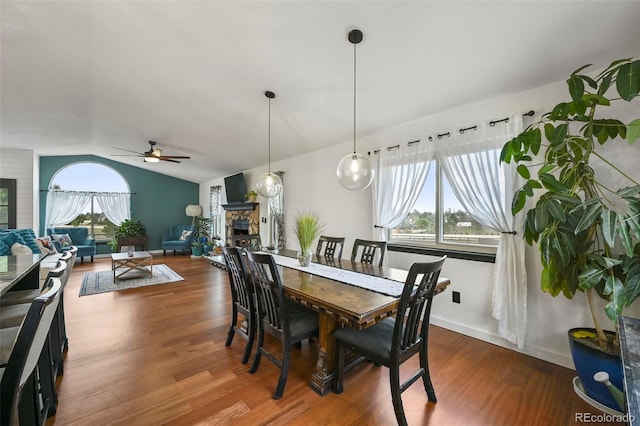 dining space with a ceiling fan, vaulted ceiling, wood finished floors, and a stone fireplace