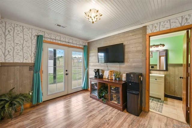 interior space with wood walls, crown molding, french doors, and light wood-type flooring