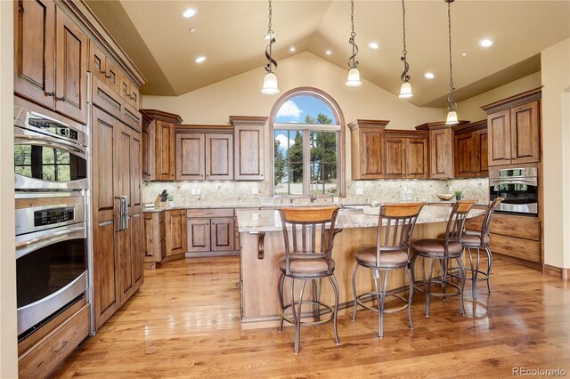 28800 Stonecrop Trl, Conifer, CO 80433 - kitchen with a center island, light stone counters, light wood-style floors, brown cabinets, and a breakfast bar