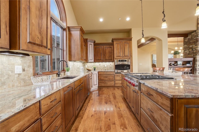28800 Stonecrop Trl, Conifer, CO 80433 - kitchen with stainless steel appliances, a sink, arched walkways, brown cabinets, and light stone counters
