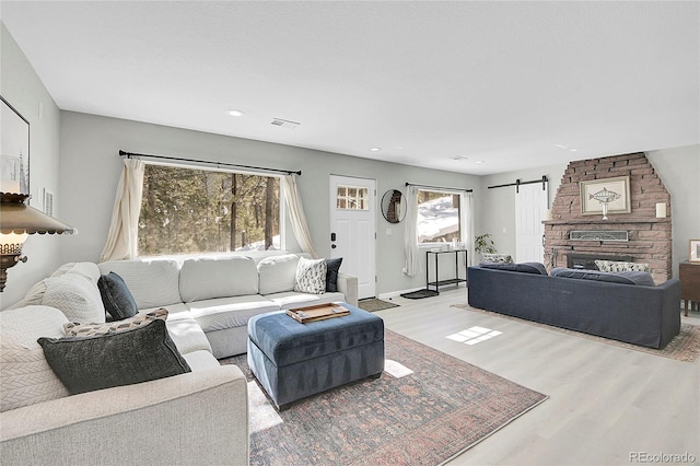 living room with a barn door, visible vents, baseboards, light wood-style floors, and recessed lighting