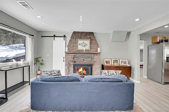 living room with visible vents, a fireplace, light wood-style flooring, and a barn door