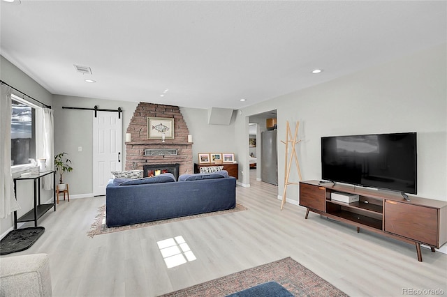 living room featuring a barn door, recessed lighting, visible vents, baseboards, and light wood-type flooring