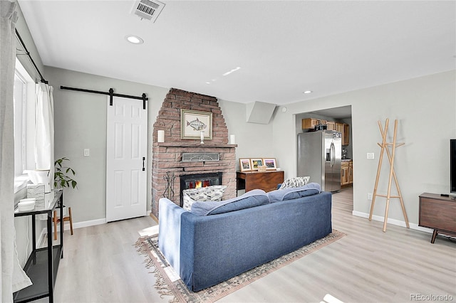 living room featuring a stone fireplace, a barn door, light wood-style flooring, and visible vents