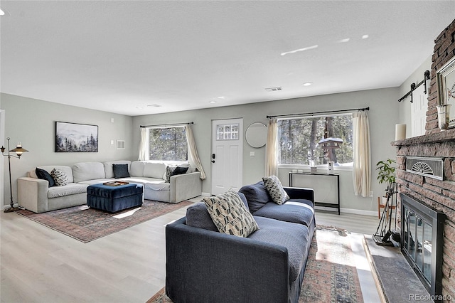 living room featuring recessed lighting, a fireplace, visible vents, baseboards, and light wood finished floors