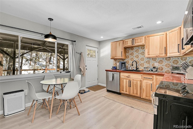 kitchen with appliances with stainless steel finishes, hanging light fixtures, a sink, light wood-style floors, and backsplash