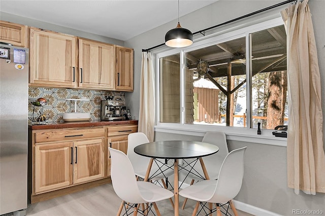 kitchen with tasteful backsplash, dark countertops, hanging light fixtures, freestanding refrigerator, and light wood-type flooring