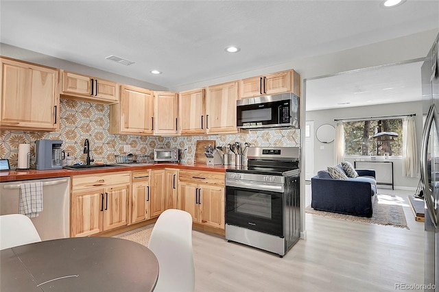 kitchen featuring stainless steel appliances, light brown cabinetry, light wood-style flooring, and visible vents