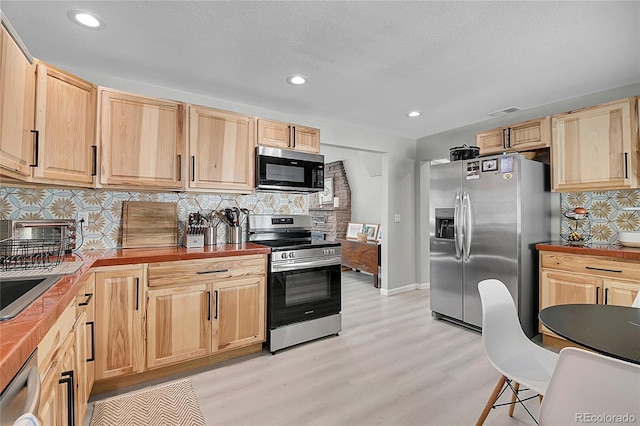 kitchen with light wood-style flooring, stainless steel appliances, butcher block countertops, decorative backsplash, and light brown cabinetry