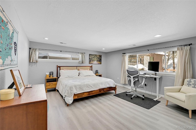 bedroom featuring light wood-type flooring, baseboards, visible vents, and a textured ceiling