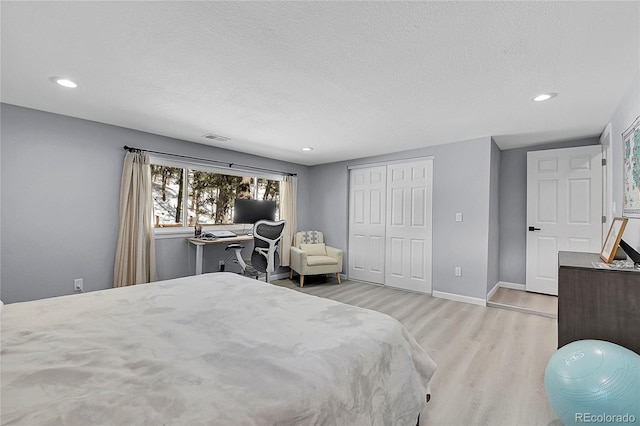 bedroom with baseboards, visible vents, a textured ceiling, light wood-type flooring, and a closet