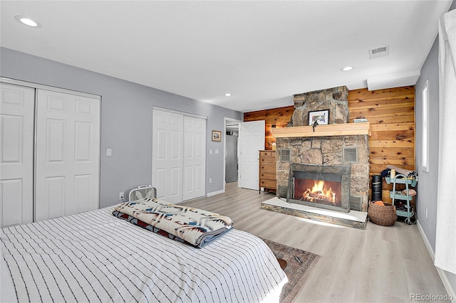 bedroom with visible vents, wood finished floors, wood walls, a fireplace, and recessed lighting