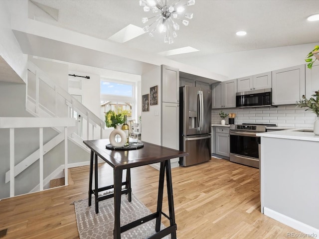 kitchen with gray cabinets, vaulted ceiling with skylight, light hardwood / wood-style floors, and appliances with stainless steel finishes