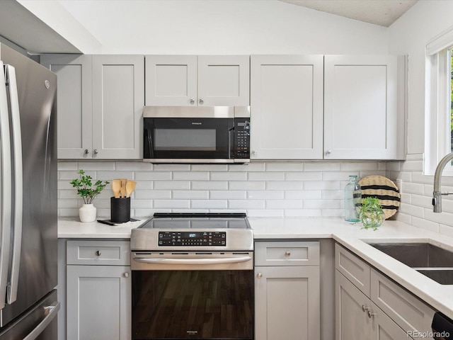 kitchen featuring stainless steel appliances, tasteful backsplash, lofted ceiling, and sink