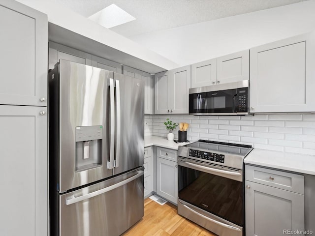 kitchen featuring appliances with stainless steel finishes, backsplash, a textured ceiling, light hardwood / wood-style flooring, and gray cabinets