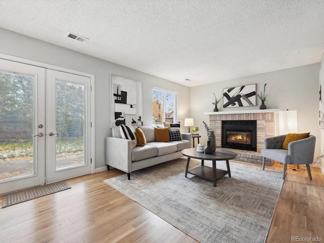 living room with a fireplace, a wealth of natural light, french doors, and light hardwood / wood-style flooring