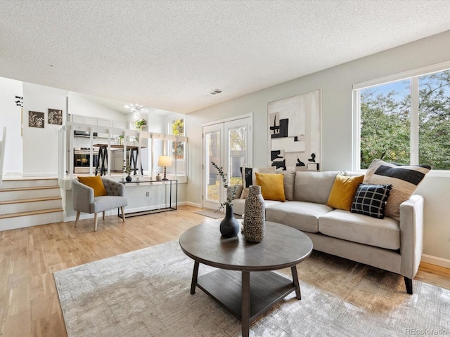 living room with a textured ceiling, light wood-type flooring, and vaulted ceiling