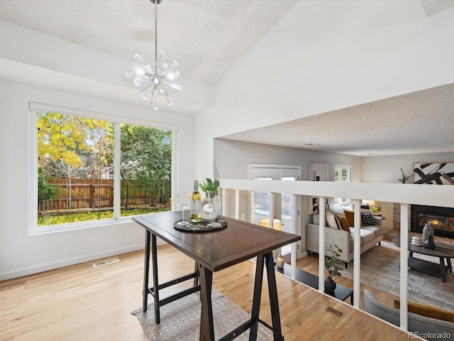 dining area with light hardwood / wood-style floors, a healthy amount of sunlight, a textured ceiling, and a chandelier