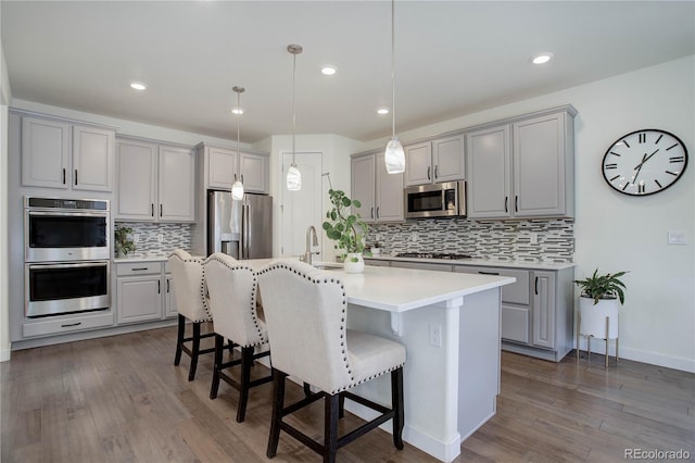 kitchen featuring gray cabinetry, a center island with sink, a breakfast bar area, appliances with stainless steel finishes, and a sink