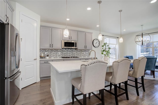 kitchen featuring gray cabinets, dark wood-style flooring, a sink, stainless steel appliances, and a kitchen breakfast bar