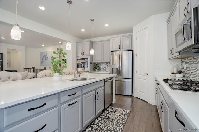 kitchen featuring gray cabinets, a sink, open floor plan, stainless steel appliances, and light countertops