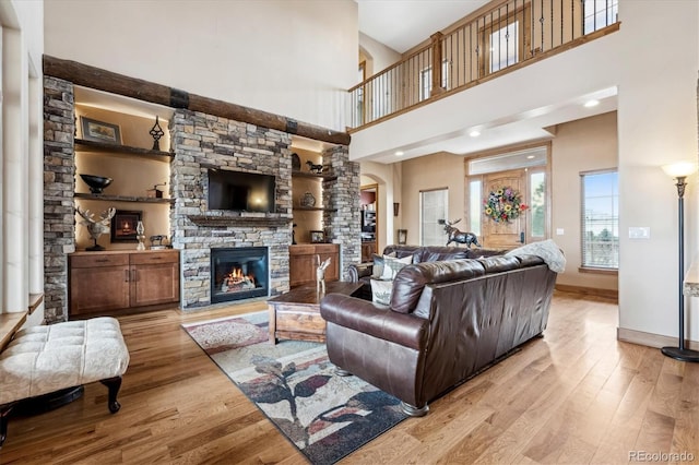 living room featuring a stone fireplace, light hardwood / wood-style flooring, and a high ceiling