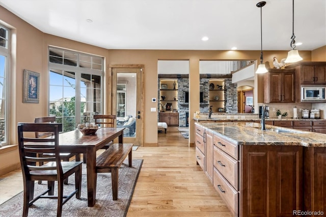 kitchen with light stone counters, tasteful backsplash, hanging light fixtures, light wood-type flooring, and stainless steel microwave