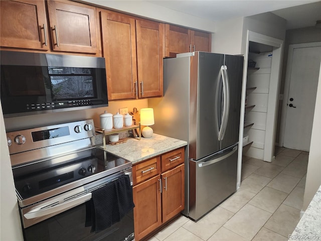 kitchen featuring light tile patterned floors, appliances with stainless steel finishes, light stone countertops, and brown cabinets