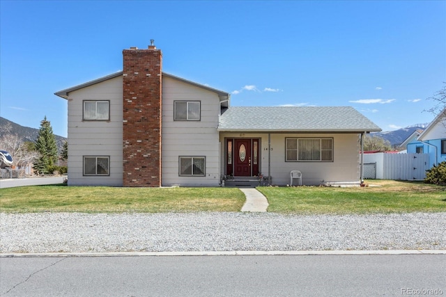 view of front of property with a chimney, roof with shingles, fence, a mountain view, and a front lawn