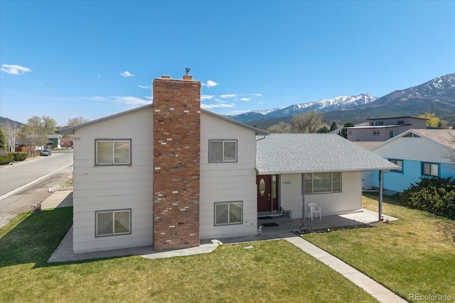 rear view of house featuring roof with shingles, a mountain view, a yard, and a chimney