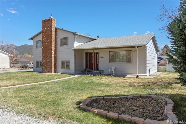 split level home with a front lawn, roof with shingles, a mountain view, and a chimney